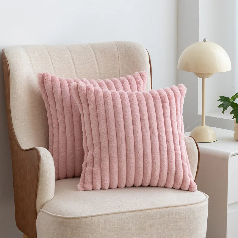 A pink faux fur stripe decorative throw pillow resting on a cream upholstered armchair.