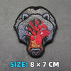 A black embroidered patch of a bear's head with red accents on a gray fabric background.