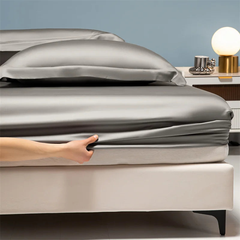 A hand is adjusting a smooth gray duvet on a bed with white sheets and a light blue wall background.