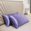 Two purple mulberry silk pillow covers resting on a light-colored headboard.