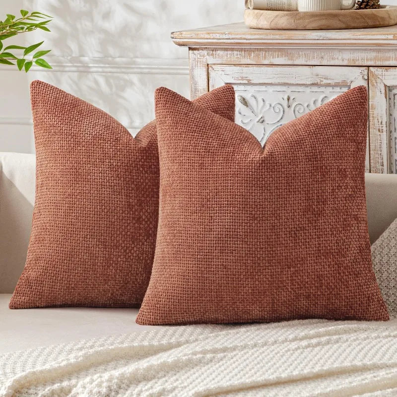 A close-up of a textured, rust-colored chenille pillow cover resting on a light-colored sofa.