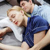 A man gently rests his head on a woman's shoulder while they lie together on a gray surface.