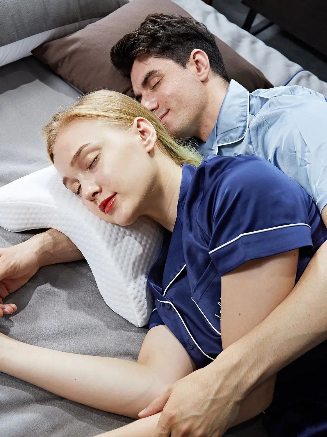 A man gently rests his head on a woman's shoulder while they lie together on a gray surface.