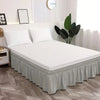 A white bed with a light gray elastic bed skirt and modern decor.