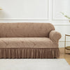 A beige jacquard stretch sofa cover featuring a leaf pattern and gathered hem, displayed on a white floor.