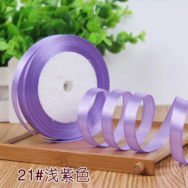 Purple satin ribbon roll with several unrolled ribbons displayed on a wooden surface.