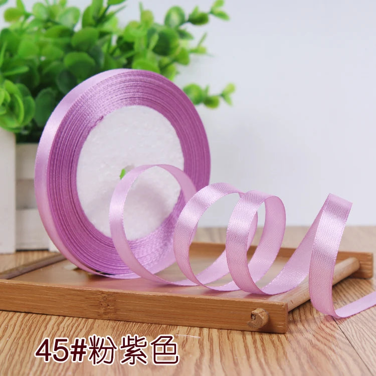 Rolls of satin ribbon in various shades of purple and pink resting on a wooden board.