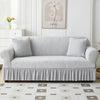 A light gray jacquard elastic sofa cover with a gathered skirt displayed on a white sofa.