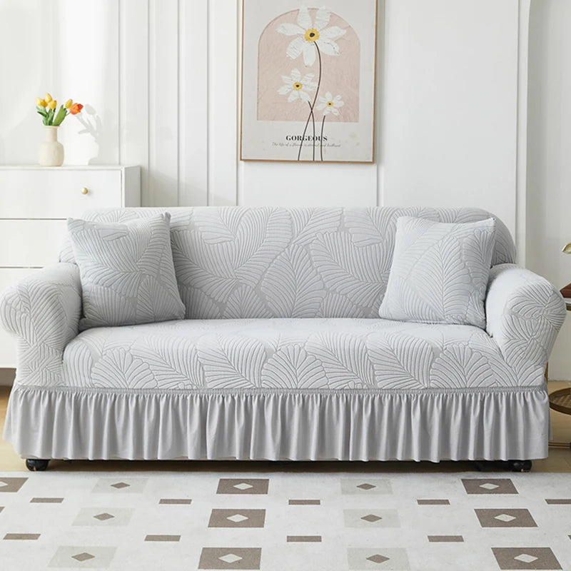 A light gray jacquard elastic sofa cover with a gathered skirt displayed on a white sofa.