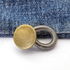 A round brass button with a silver spring mechanism resting on a dark denim fabric.