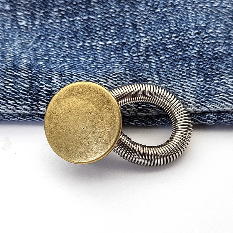 A round brass button with a silver spring mechanism resting on a dark denim fabric.