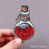 An embroidered patch depicting a jar with a cork stopper and a monster head inside, featuring red and blue stitching.