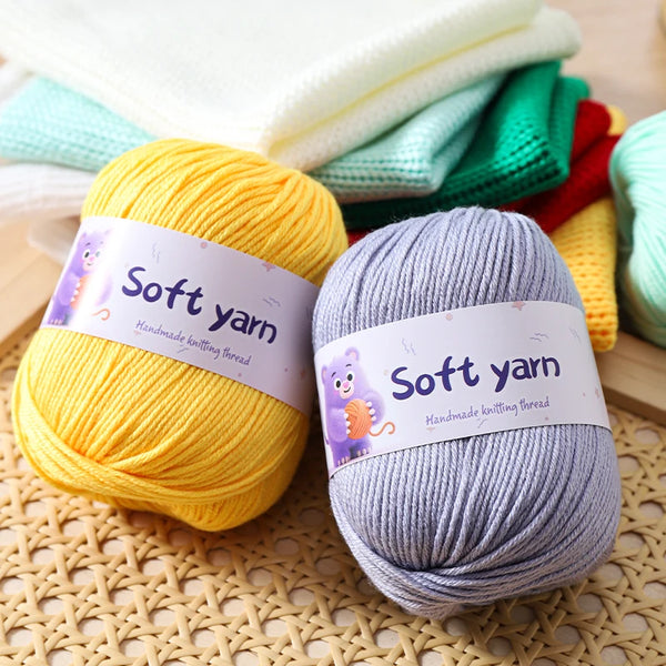 A stack of soft yellow and gray hand knitting yarn skeins resting on a woven mat.