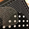 A clear acrylic quilting ruler with corner templates is shown on a black background with a grid and measurement markings.