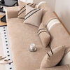 A beige chenille sofa protector cover with black stripes and decorative pillows on a light-colored sofa.
