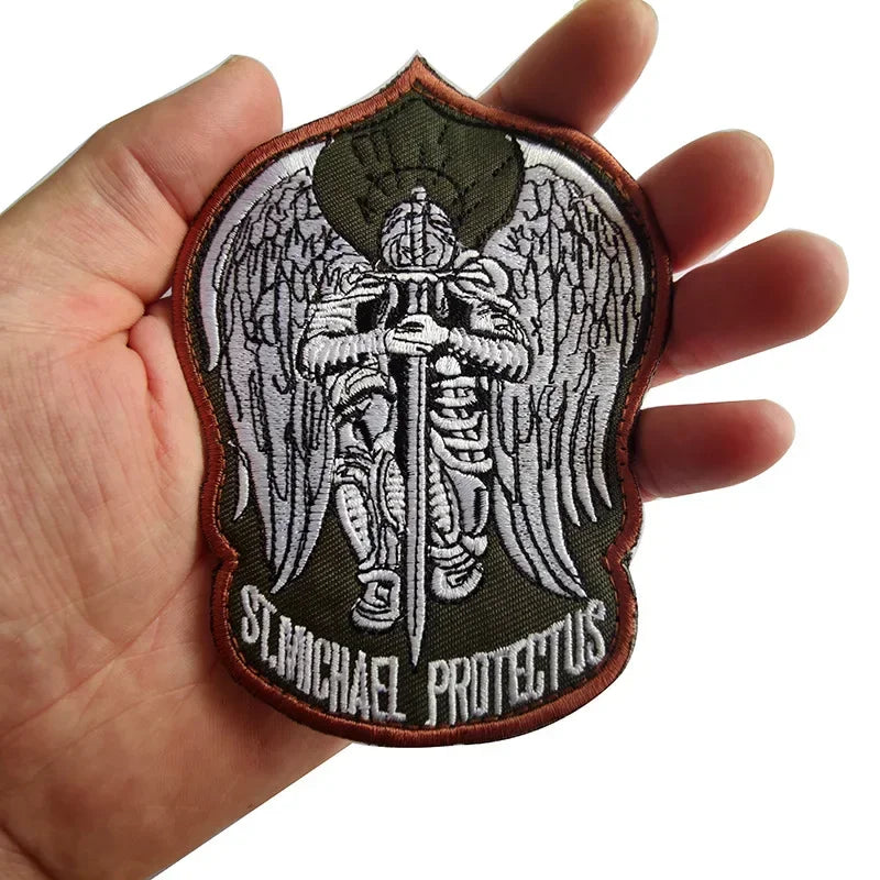An embroidered angel patch featuring a winged figure and the text St. Michael Protectus on dark green fabric.