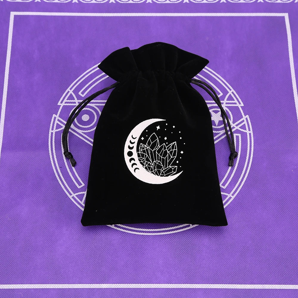 A black velvet pouch with a crescent moon and crystal design is displayed on a purple surface.