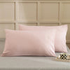 A set of solid pink microfiber pillow covers displayed on a bed with a light neutral headboard.