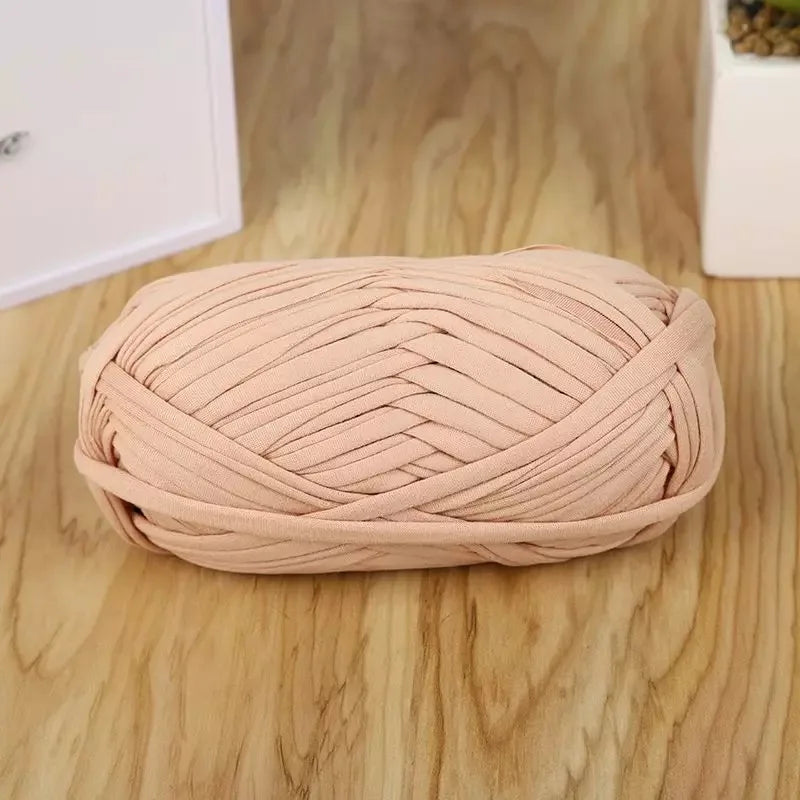A ball of light pink flat thread yarn for crafting and sewing resting on a wooden surface.