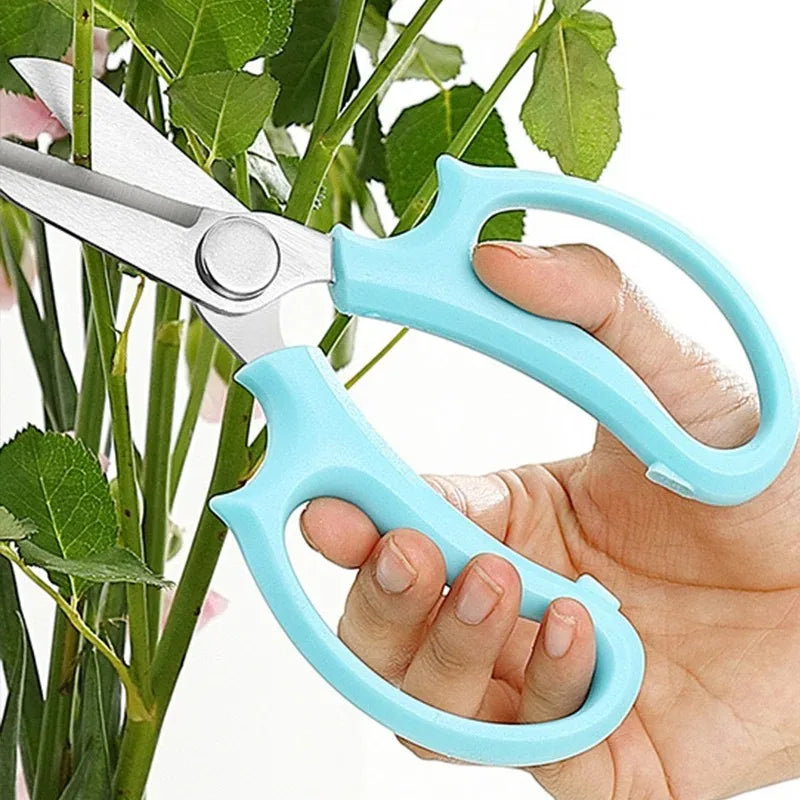 A hand holds a light blue precision shears used to trim plant branches.