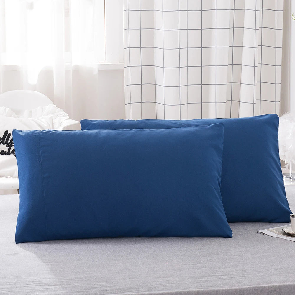 A stack of solid navy blue microfiber pillow covers resting on a gray bed sheet.