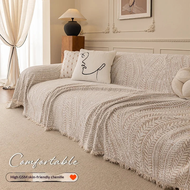 A beige herringbone chenille sofa cover draped over a light-colored sofa with decorative pillows.