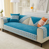 A vibrant blue quilted sofa cover with lace trim and patterned accents displayed on a light-colored sofa.