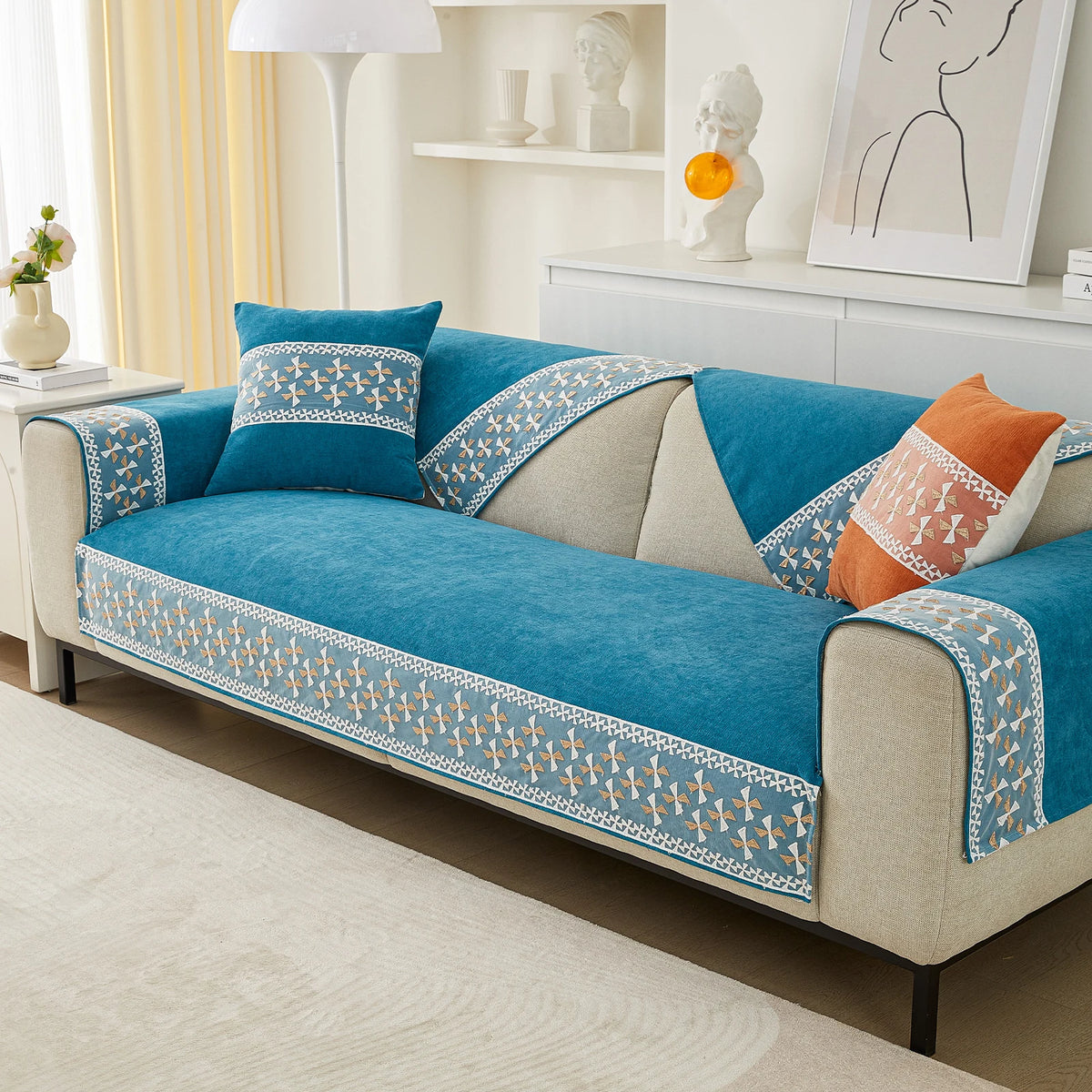 A vibrant blue quilted sofa cover with lace trim and patterned accents displayed on a light-colored sofa.