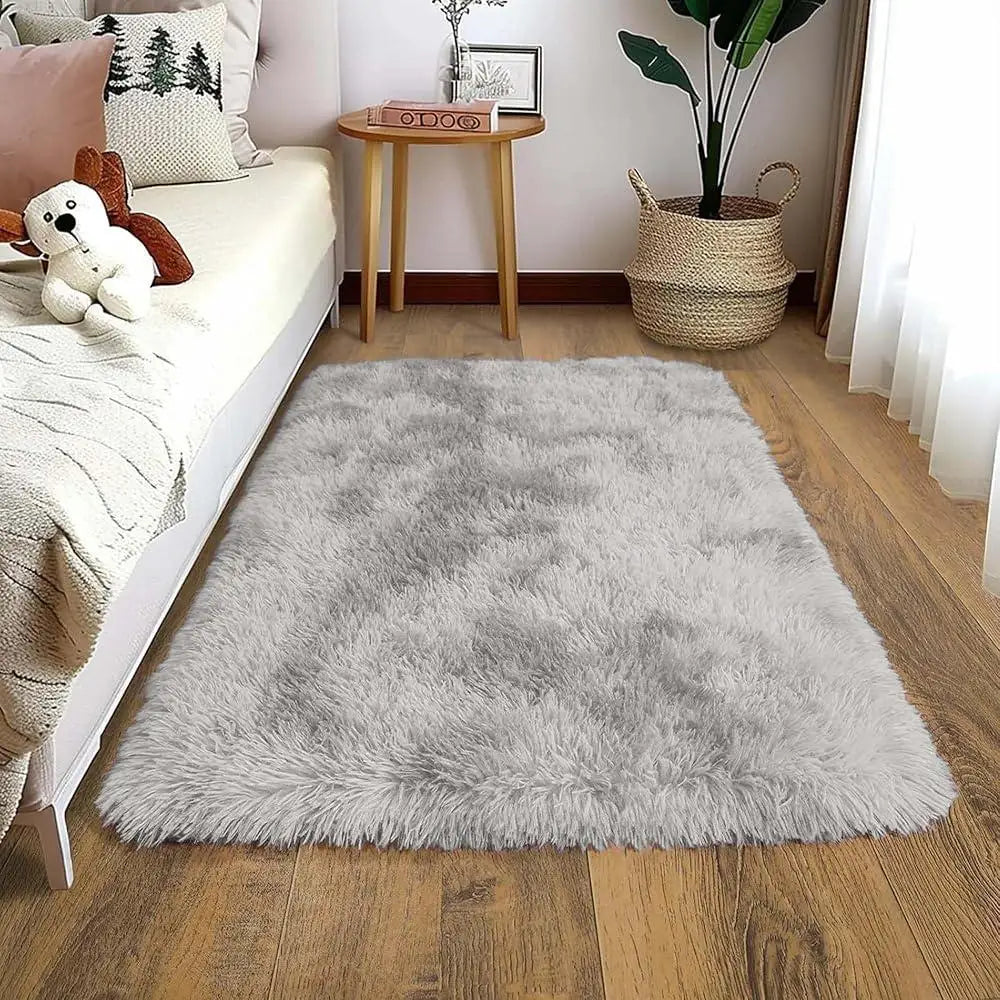 A fluffy gray plush area rug placed on a light wood floor next to a bed.