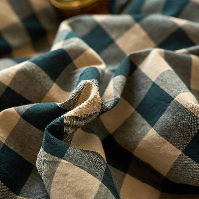 A close-up of a hand-dyed cotton plaid fabric in shades of teal, gray, and beige, folded and draped.
