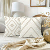 A close-up of a white decorative pillow cover with a geometric pattern on a light gray sofa.