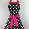 A black polka dot apron with pink ruffled trim and a large pink bow displayed on a mannequin.