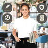 A smiling woman wearing a white polo shirt and black apron, holding a silver teapot.