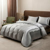 A bed dressed with a satin gray duvet and pillows in a bedroom setting.