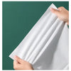 A hand is holding a white disposable compressed fiber face towel against a dark green background.