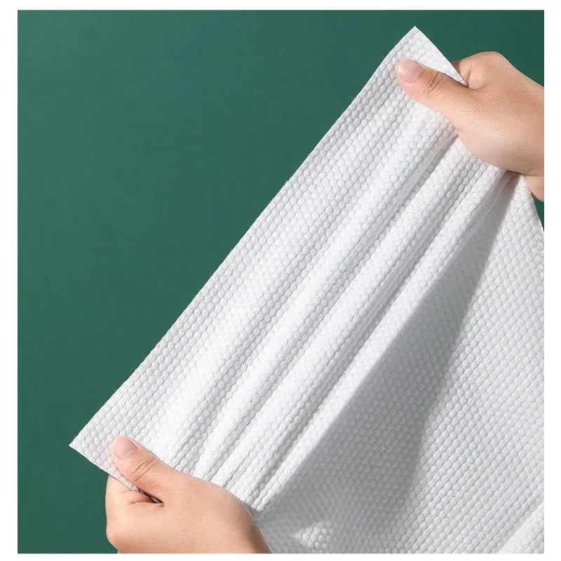 A hand is holding a white disposable compressed fiber face towel against a dark green background.