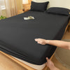 A dark gray fitted bed sheet is draped over a wooden bed frame, with a hand adjusting the fabric.