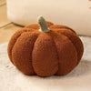 A round, textured brown plush pumpkin throw pillow with a small green stem.