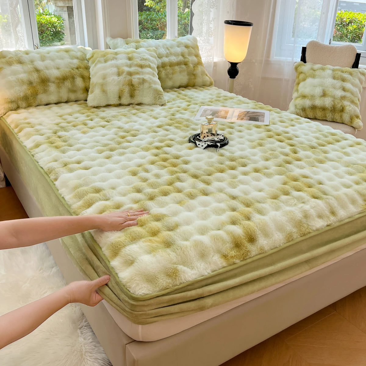 A luxury faux rabbit fur fitted sheet set in pale green and cream colors displayed on a bed.