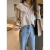A woman wearing a cream retro lace long sleeve blouse and light wash jeans, standing in front of a mirrored cabinet.