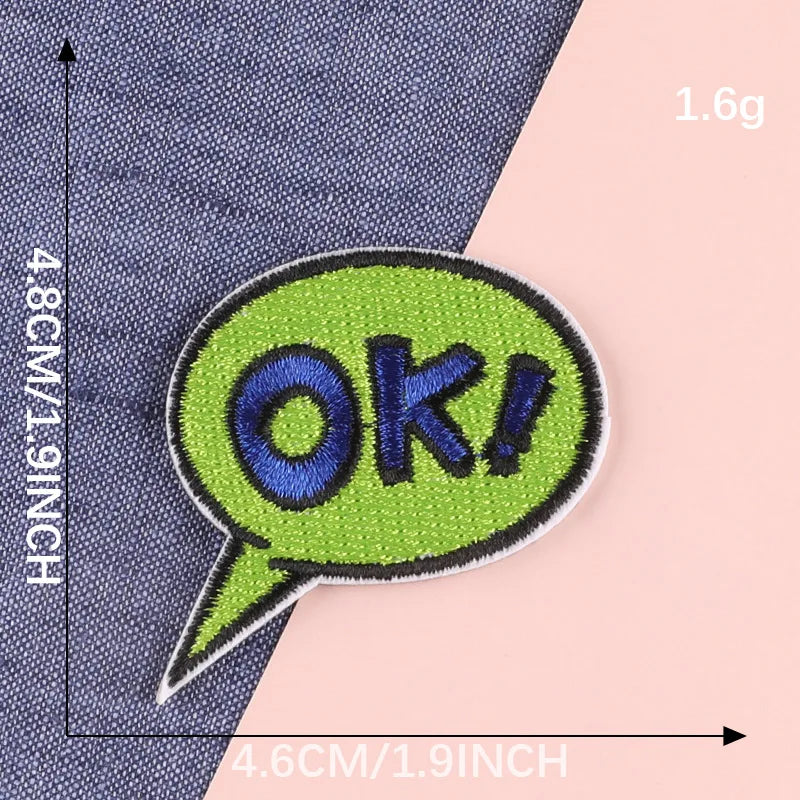 A bright lime green embroidery patch shaped like a speech bubble with the text OK! sewn onto a dark blue fabric.