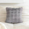 A gray plush faux rabbit fur decorative throw pillow resting on a white leather sofa.