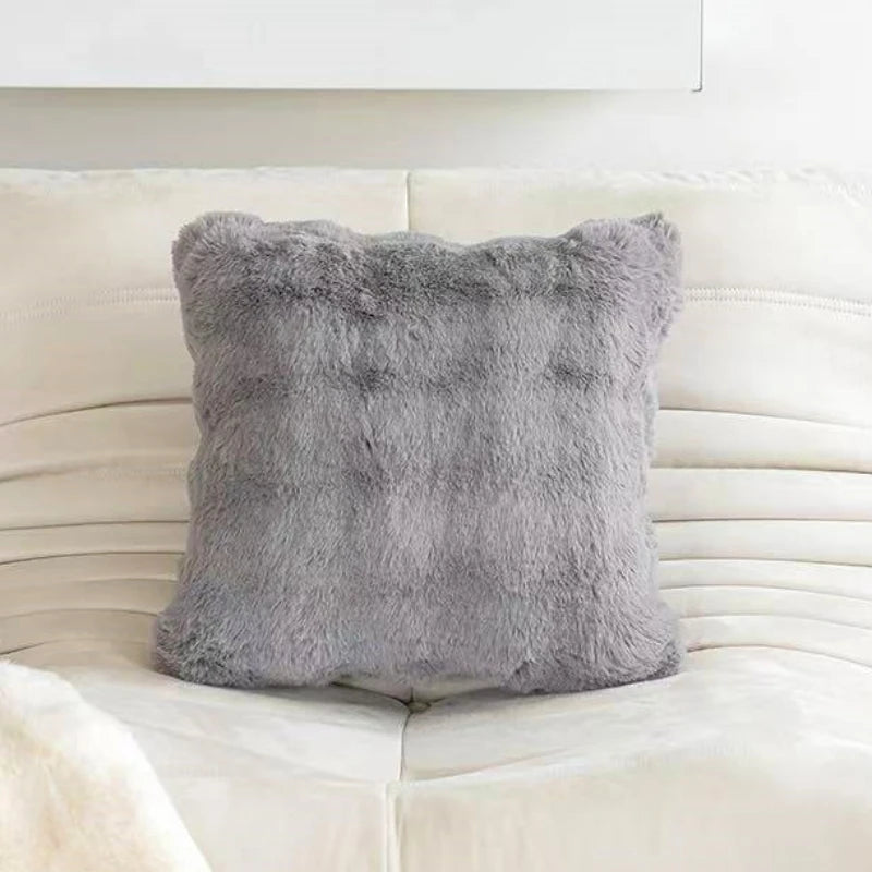 A gray plush faux rabbit fur decorative throw pillow resting on a white leather sofa.