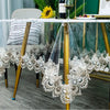 White lace embroidered PVC tablecloth draped over a gold stand on a wooden table.