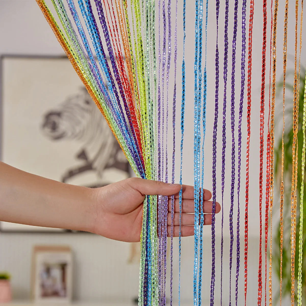 A hand is holding colorful decorative door string curtains with various strands of rainbow colors.