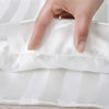 A hand is holding a white satin pillow cover with subtle stripes.