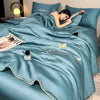 A teal ice silk fiber summer quilt draped over a bed, with a person resting on it and a perfume bottle visible.