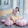A woman sits on the floor surrounded by numerous orange and white pumpkin plush cushions.