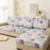 A floral print elastic sofa protective cover featuring purple and green leaves on a beige sofa.