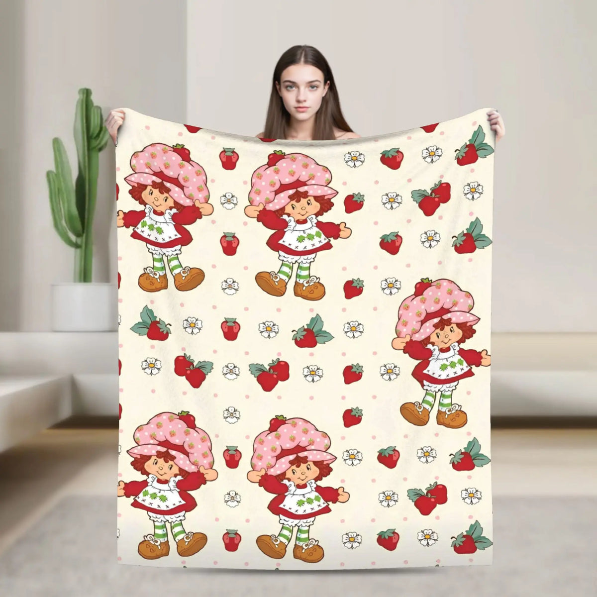 A woman is holding a strawberry shortcake plush throw blanket featuring cute characters and strawberries on a light backgroun